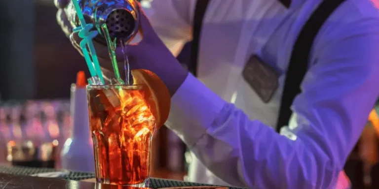 Imagem mostra um barman a preparar um drink no balcão de um bar.