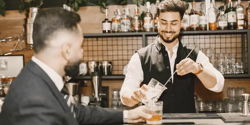 Barman com um sorriso no rosto faz um drink para o cliente
