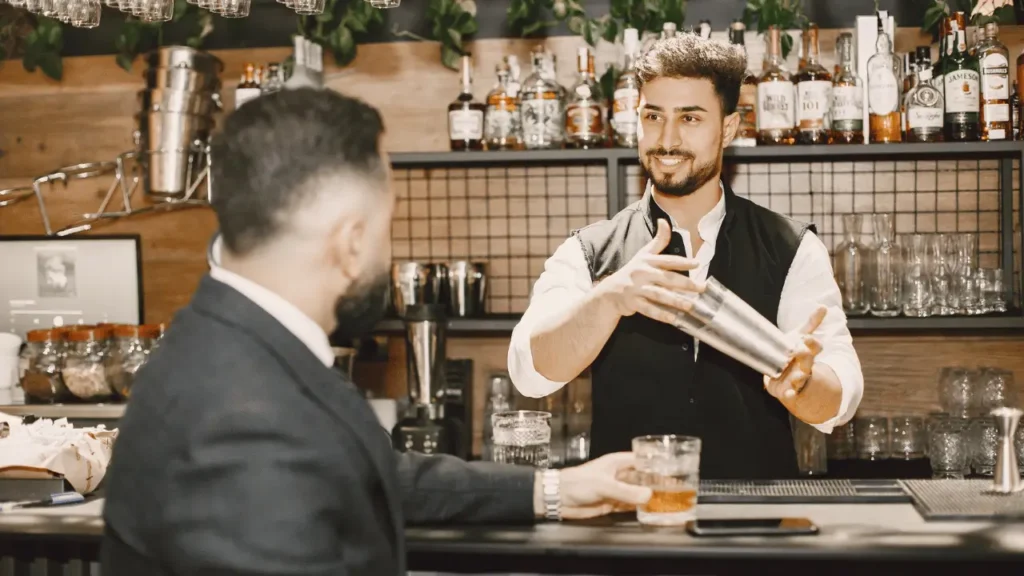 Bartender fazendo um cocktail com um sorriso na cara enquanto estás a conversar com um cliente no bar