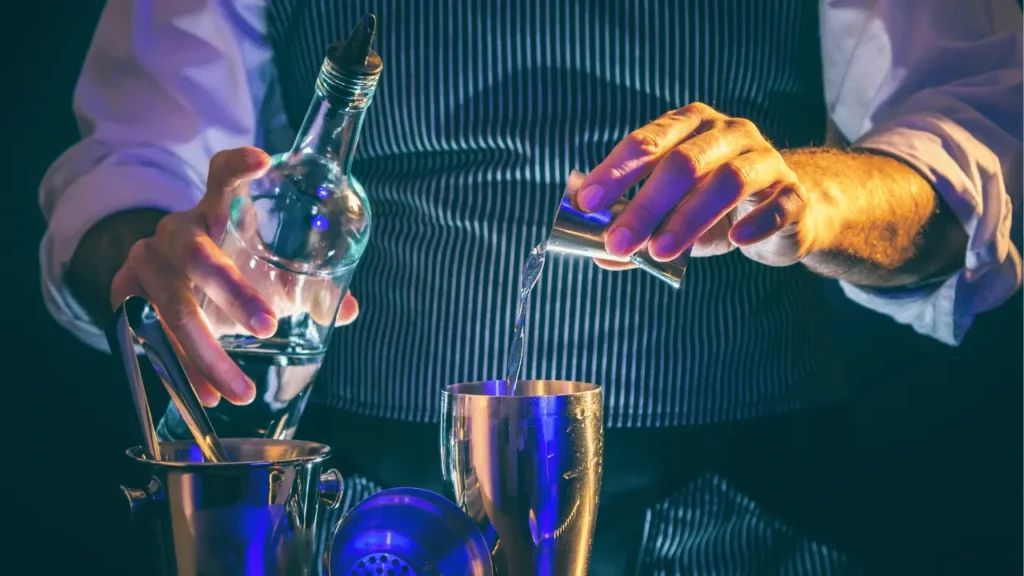 imagem de um barman derramando o líquido para o shaker e uma garrafa de bebida na outra mão