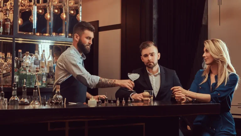 Imagem mostra barman servindo um drink para uma cliente. Ambos são brancos.