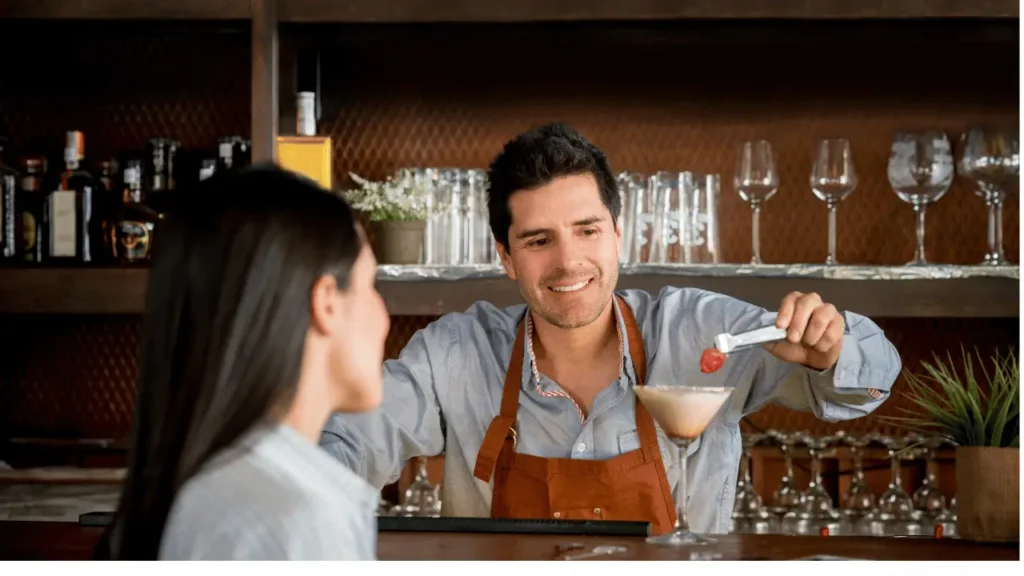 Barman está servindo um cocktail para uma cliente. Os dois são brancos.