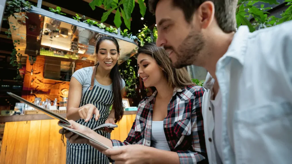 Dois clientes, um homem e uma mulher, olham o menu e a atendente ao lado.